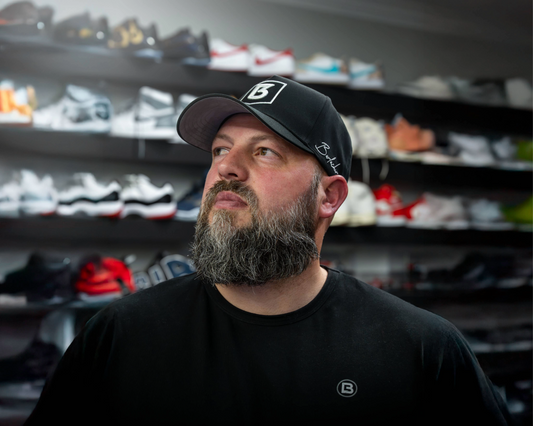 Man wearing a black cap with a logo in front of shelves filled with various shoes.