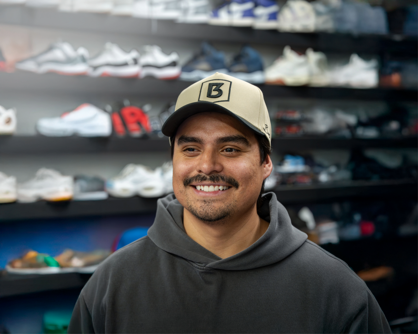 Man wearing a cap and hoodie in front of shelves displaying various shoes